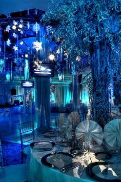 a table is set up for an event with blue lighting and snowflakes hanging from the ceiling