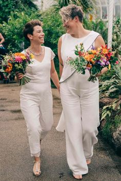 two women in white outfits holding hands and walking down the street with flowers on their laps