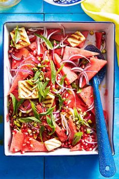 watermelon and onion salad in a white bowl with blue serving spoons on the side