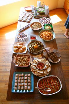 a long table filled with lots of food on top of a hard wood floored floor