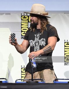 a man with long hair and a hat holding a cell phone in one hand while standing on a stage