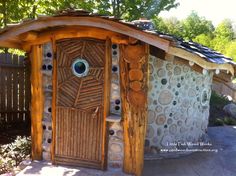 an outdoor toilet made out of rocks and wood with eyes on the door, in front of a fence