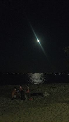 two people are sitting on the beach at night