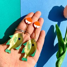 a person holding two fish shaped brooches in their hand next to a flower