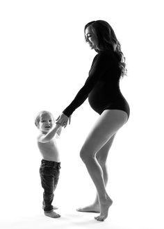 a woman holding the hand of a little boy in front of a white background with one leg up