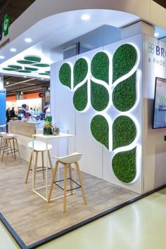 an exhibit booth with green plants on the wall and stools in front of it