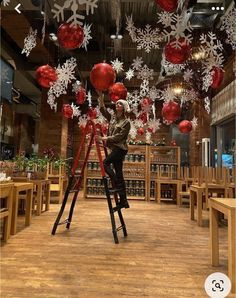 a man on a ladder with red balls and snowflakes hanging from the ceiling