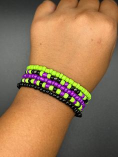 a person's hand with a bracelet made out of neon green, purple and black beads