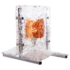 an ice cube with a lit candle inside it on a metal stand against a white background