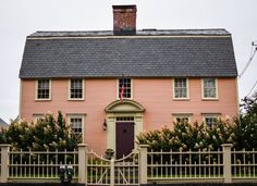 a pink house with a black roof and white picket fence in front of it on a cloudy day