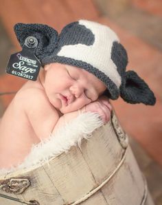 a baby sleeping in a bucket wearing a hat