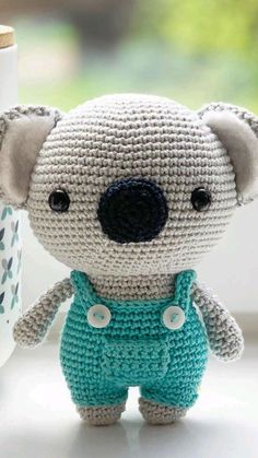 a crocheted koala bear sitting next to a cup