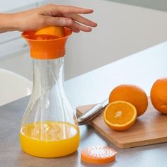 someone is squeezing orange juice into a glass pitcher on a cutting board next to sliced oranges