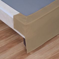 an image of a bed that is in the middle of wood flooring and has a sheet on it