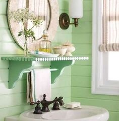 a bathroom with green walls and a white sink under a round mirror on the wall