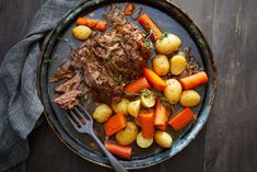 a plate with meat, potatoes and carrots next to a fork on a wooden table