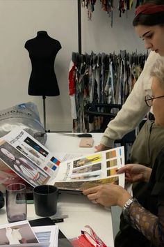 two women sitting at a table working on an item in front of a mannequin