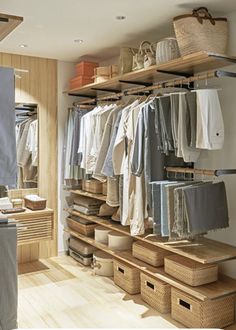 an open closet with clothes hanging on shelves and baskets in the bottom row, next to a laundry hamper