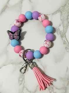 a pink, blue and purple bracelet with a butterfly charm on the end is sitting on a marble surface