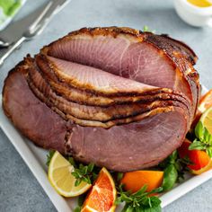 sliced ham sitting on top of a white plate next to oranges and lemon wedges