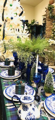 the table is set with blue and white dishes, place settings, and christmas trees