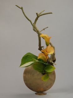 a vase filled with yellow flowers on top of a white table next to a tree branch