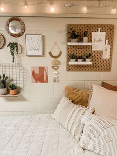 a white bed topped with lots of pillows next to a wall filled with potted plants