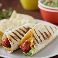 two hotdogs with mustard and guacamole are on a plate next to chips