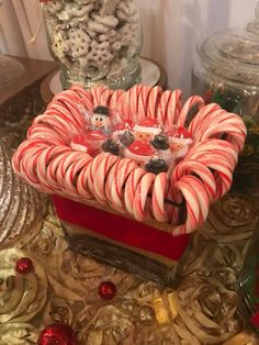 some candy canes are in a red box on a table next to other candies