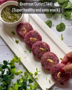 someone is holding up some food on a white plate with green leaves and sauce in the background