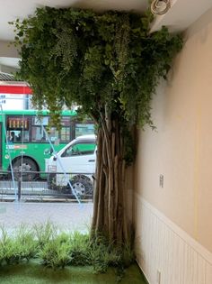 a green bus parked next to a tree in the middle of a parking garage area