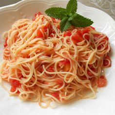 a white plate topped with pasta and sauce covered in tomato sauce, garnished with mint