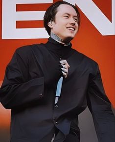 a man in a black shirt and tie standing next to a sign with the letter en on it