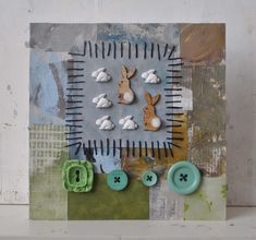 an altered collage with buttons and bunny ears on it's side, in front of a white wall