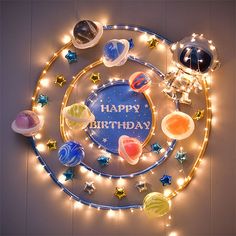 a happy birthday sign with planets and stars on the wall above it, surrounded by string lights