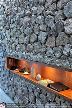 a stone wall with books and vases on the shelf next to it, along with other items