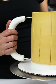 a woman is holding a yellow and white cake on a silver platter with a plastic handle