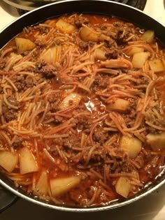 a skillet filled with meat and noodles on top of a stovetop oven next to a pot of soup