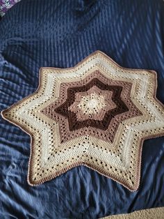 a crocheted star on a bed with blue sheets and purple bedspread