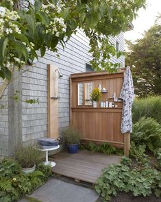 an outdoor shower in the middle of a garden with flowers and plants around it, next to a wooden deck