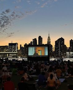 people sitting on the grass watching a movie in front of a city skyline at night