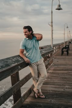 a man standing on a wooden pier next to the ocean with his arm around his neck