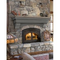 a stone fireplace in a living room next to a couch and table with a lamp on it