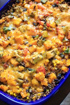 a blue casserole dish filled with vegetables and cheese on a wooden table top