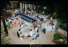 a group of people sitting at tables in front of a swimming pool with white tablecloths