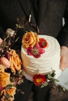 a person holding a cake with flowers on it