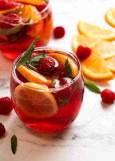 two glasses filled with fruit and garnish next to sliced oranges