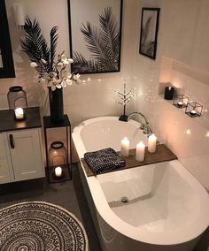 a white bath tub sitting in a bathroom next to two candles and pictures on the wall