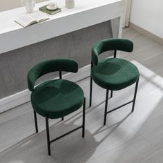 two green chairs sitting next to each other in front of a white counter with a book on it