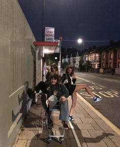 three people sitting on a bench in front of a building at night with the lights on